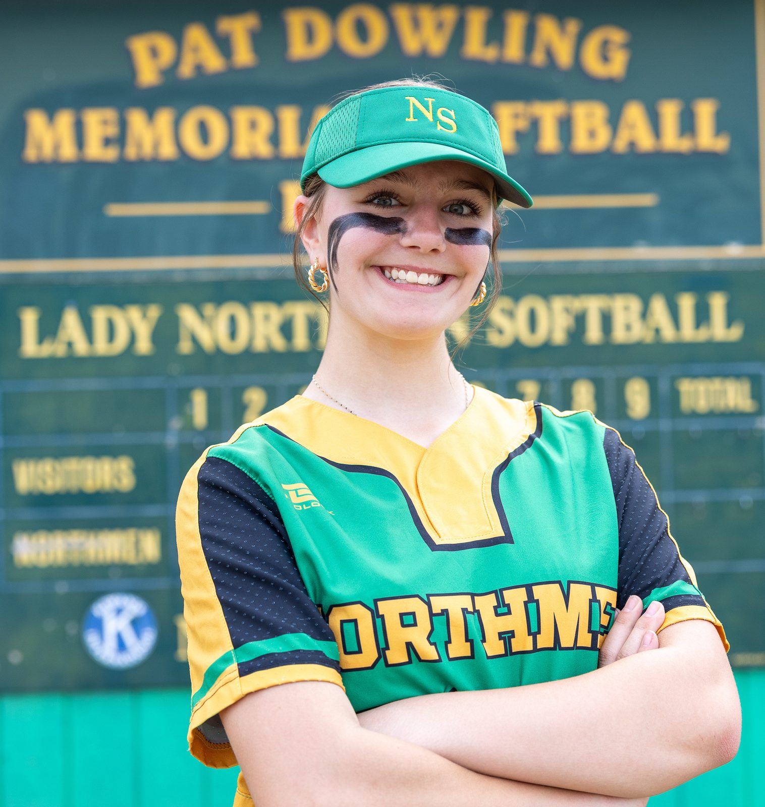 Smiling softball player in eye black in front of the scoreboard