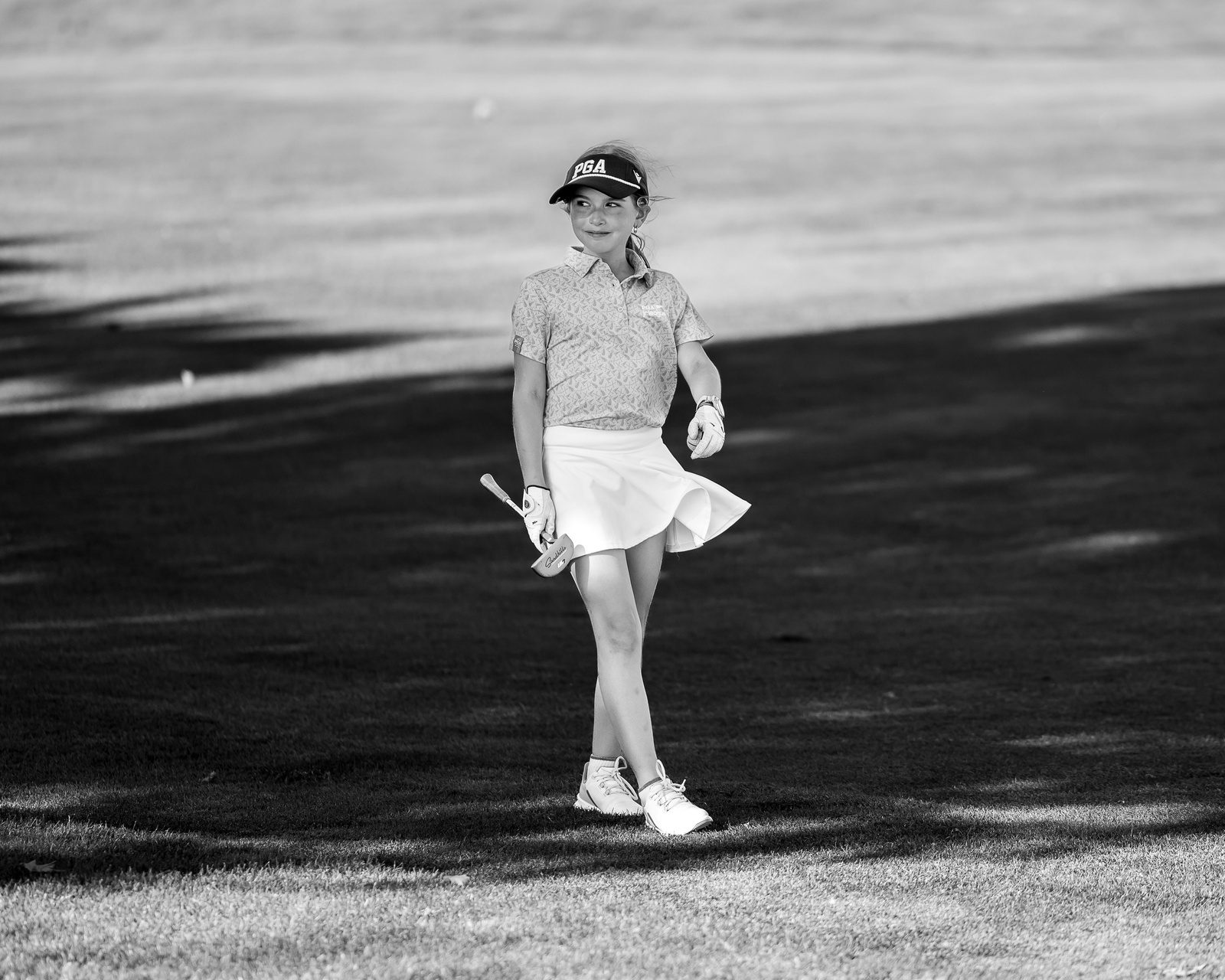 Black-and-white photo of a young golfer walking the fairway